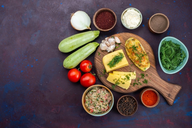 Vue de dessus des courges cuites au four avec assaisonnements de fromage verts, viande et légumes frais sur le bureau sombre.