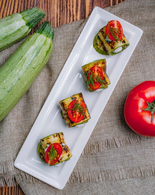 Vue de dessus des courgettes grillées avec des feuilles de fromage à la crème et des tomates sur la table