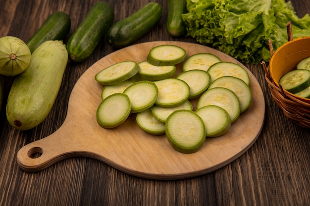 Vue de dessus des courgettes hachées isolé sur une planche de cuisine en bois avec des concombres et de la laitue isolé sur un fond en bois