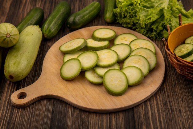 Vue de dessus des courgettes hachées isolé sur une planche de cuisine en bois avec des concombres et de la laitue isolé sur un fond en bois