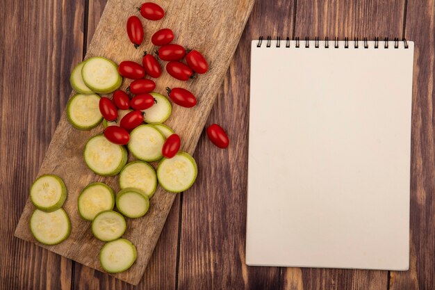 Vue de dessus de courgettes hachées riches en vitamines sur une planche de cuisine en bois avec des tomates cerises sur un fond en bois avec espace copie