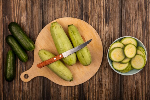 Vue de dessus des courgettes isolées sur une planche de cuisine en bois avec un couteau avec des concombres isolés sur une surface en bois