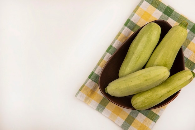 Vue de dessus des courgettes vertes fraîches sur un bol sur un chiffon vérifié sur un fond blanc avec copie espace