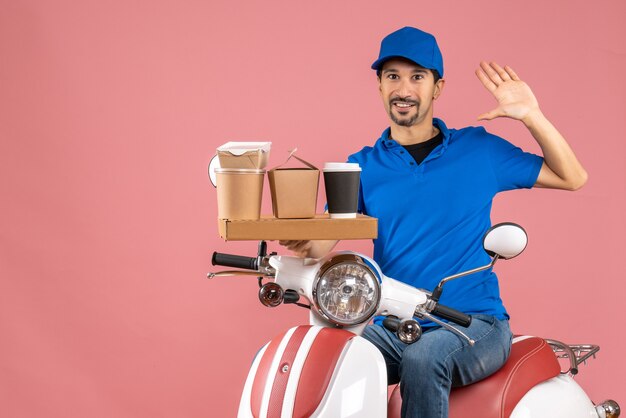 Vue de dessus d'un coursier souriant portant un chapeau assis sur un scooter montrant cinq sur une pêche pastel