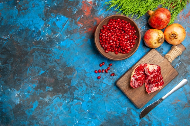 Photo gratuite vue de dessus un couteau de dîner à la grenade coupé sur une planche à découper des graines de grenade dans un bol et des grenades sur fond bleu