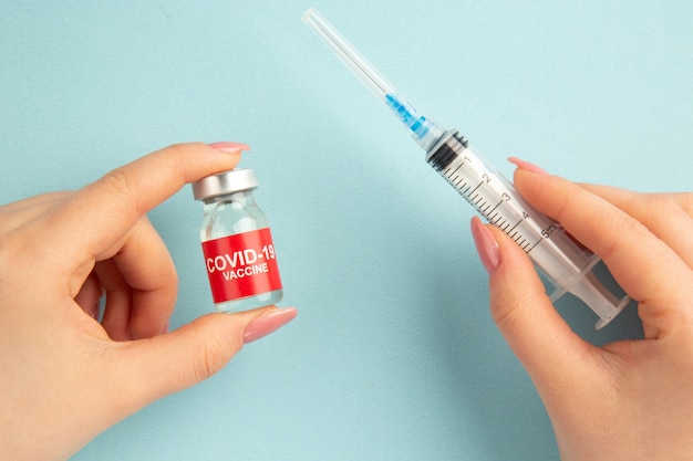 Vue de dessus covid- vaccin dans les mains des femmes avec injection sur fond bleu laboratoire pandémique covid- science hôpital virus santé couleur