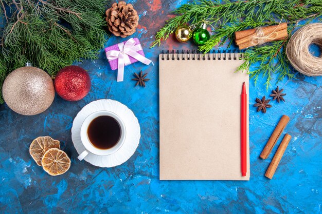 Vue de dessus crayon rouge sur un cahier des branches d'arbres de pin une tasse de surface bleue teaon