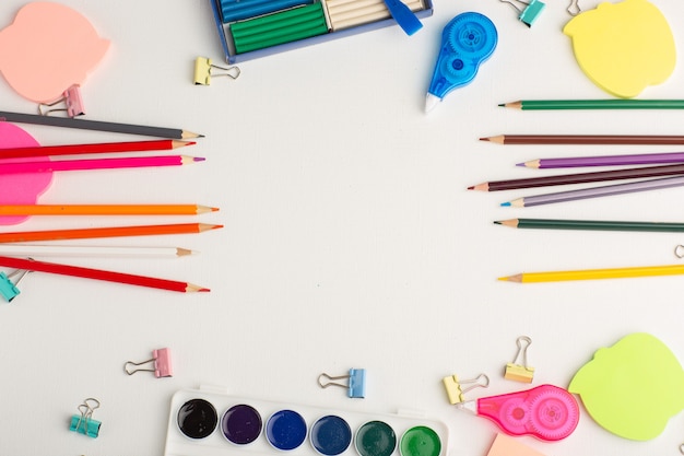 Vue de dessus crayons colorés avec des peintures et des autocollants sur la peinture de couleur de dessin d'art de bureau blanc