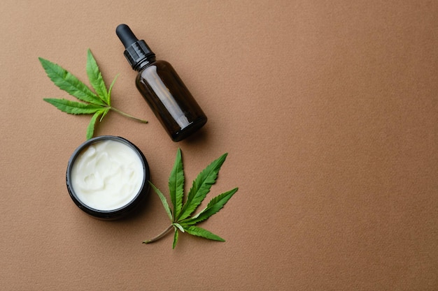 Vue de dessus de la crème à l'huile cosmétique de cannabis dans une bouteille de pot et une feuille de plante verte Cosmétique naturel sur fond marron Espace de copie plat
