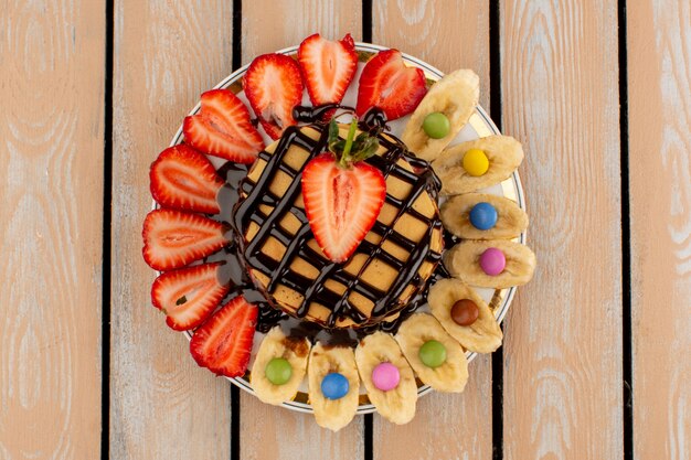 Vue de dessus des crêpes au chocolat avec des fraises rouges en tranches et des bananes sur le plancher en bois