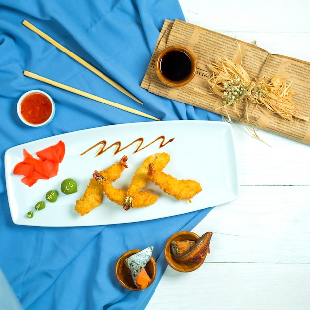 Vue de dessus des crevettes tempura servies avec du gingembre et du wasabi sur un plateau bleu et blanc