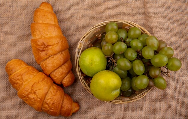 Vue de dessus des croissants et panier de raisin et pluots sur fond de sac