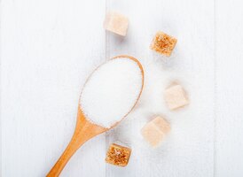 Photo gratuite vue de dessus d'une cuillère en bois avec du sucre blanc et du sucre en poudre sur fond blanc