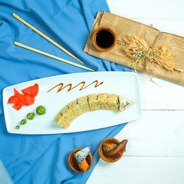 Vue de dessus de la cuisine japonaise traditionnelle sushi rollwith riz crevettes avocat et fromage à la crème servi avec sauce soja gingembre et wasabi sur bleu et blanc