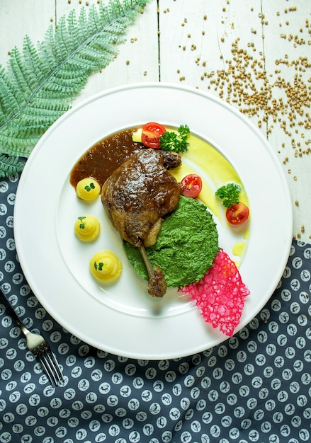 Vue de dessus de la cuisse de canard rôti avec sauce à l'avocat et purée de pommes de terre aux tomates cerises sur une plaque blanche