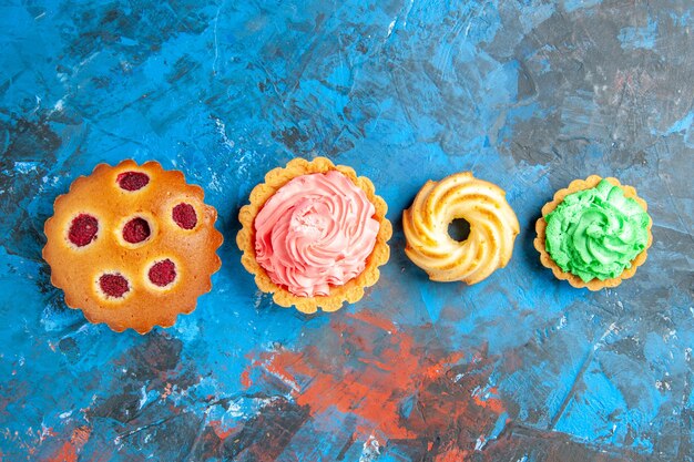 Vue de dessus des cupcakes aux framboises de la rangée horizontale, petites tartes et biscuits sur la surface bleue