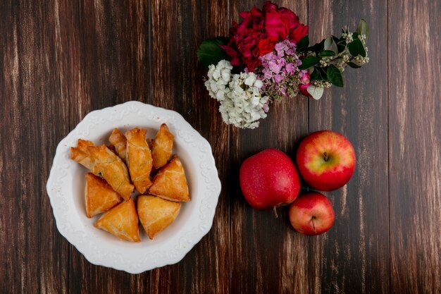 Vue de dessus curabier sur une assiette avec des pommes rouges et des fleurs sur un fond en bois