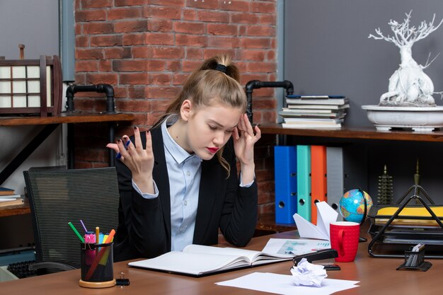 Vue de dessus d'une dame confuse assise à une table et concentrée sur quelque chose avec soin au bureau