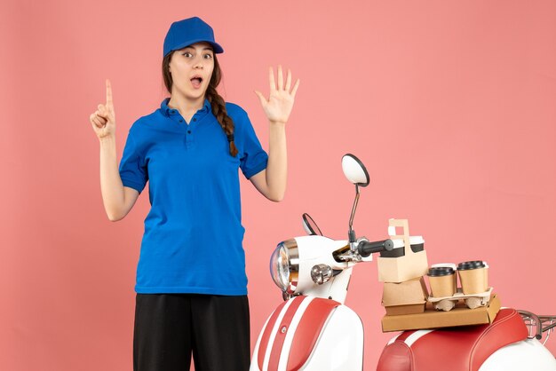 Vue de dessus d'une dame de messagerie debout à côté d'une moto avec du café et des petits gâteaux dessus montrant cinq pointant vers le haut sur fond de couleur pêche pastel