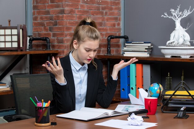 Vue de dessus d'une dame surprise assise à une table et concentrée sur quelque chose avec soin au bureau