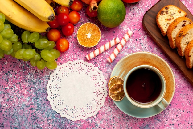 Photo gratuite vue de dessus délicieuse composition de fruits avec des gâteaux en tranches et une tasse de thé sur un bureau rose clair