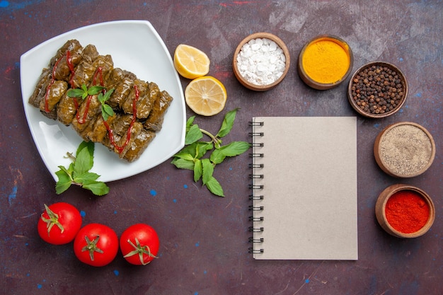 Photo gratuite vue de dessus délicieuse feuille dolma avec assaisonnements au citron et tomates sur fond sombre plat feuille dîner nourriture viande