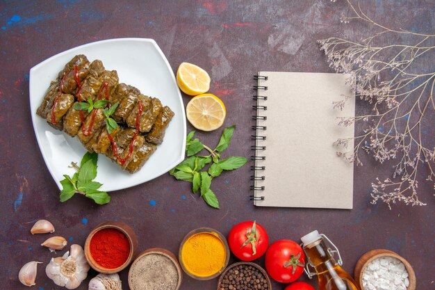 Vue de dessus délicieuse feuille dolma avec assaisonnements au citron et tomates sur un plat de bureau sombre feuille nourriture viande dîner