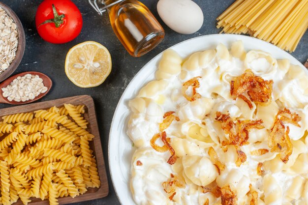 Vue de dessus de la délicieuse pâte cuite avec des assaisonnements de légumes pour pâtes crues et des œufs sur une table sombre