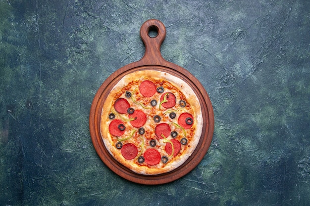 Vue de dessus de la délicieuse pizza sur une planche à découper en bois sur une surface bleu foncé