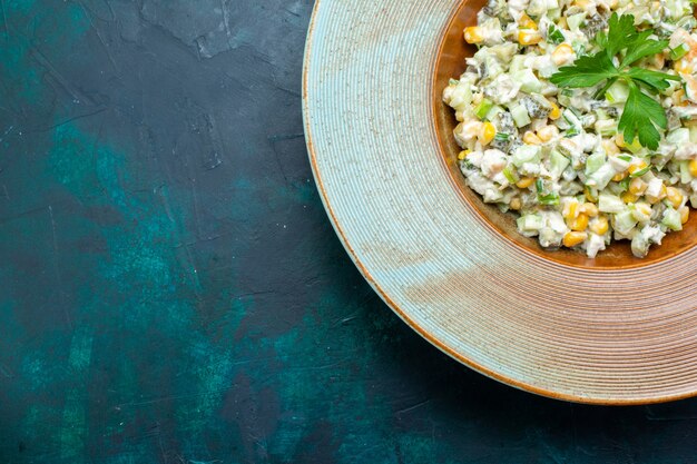 Vue de dessus délicieuse salade à l'intérieur d'une assiette ronde sur le bureau bleu foncé.