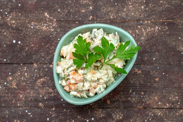 Vue de dessus délicieuse salade mayyonaise à l'intérieur de la plaque verte avec du vert sur le brun woode bureau salade alimentaire repas collation photo