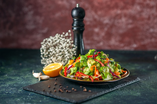 Vue de dessus d'une délicieuse salade végétalienne avec des ingrédients frais dans une assiette et du poivre sur une planche à découper noire