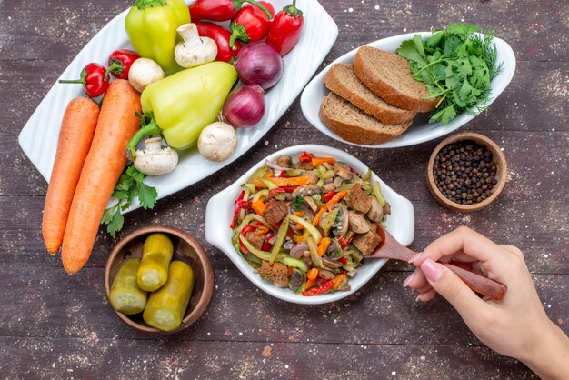 Vue de dessus de la délicieuse salade de viande avec de la viande en tranches et des légumes cuits avec du pain de cornichons sur brun, plat de viande