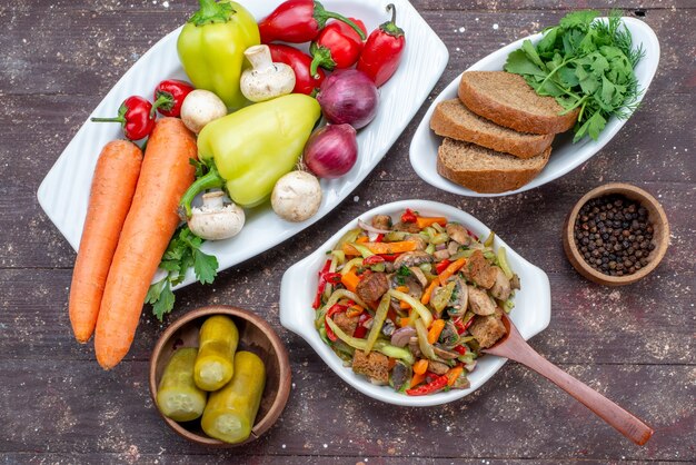 Vue de dessus de la délicieuse salade de viande avec de la viande en tranches et des légumes cuits avec du pain de cornichons sur un bureau brun, de la viande de plat de repas alimentaire