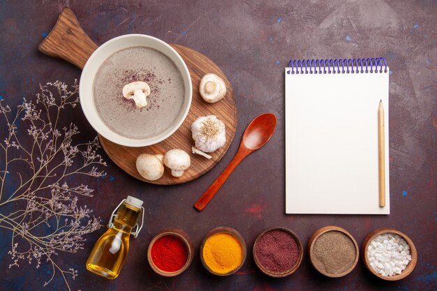 Vue de dessus délicieuse soupe aux champignons avec différents assaisonnements sur un bureau sombre