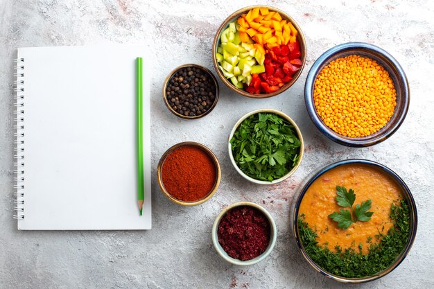 Vue de dessus délicieuse soupe aux haricots avec différents assaisonnements sur une surface blanche