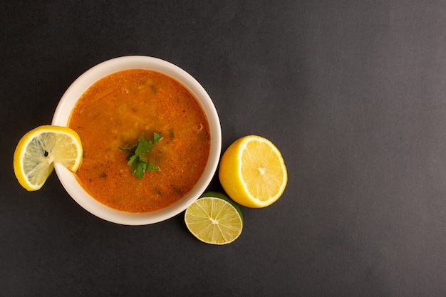 Vue de dessus de la délicieuse soupe aux légumes à l'intérieur de la plaque avec du citron sur la surface sombre