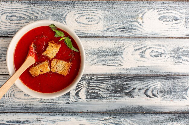 Vue de dessus délicieuse soupe aux tomates avec des biscottes à l'intérieur sur la table grise, souper repas dîner