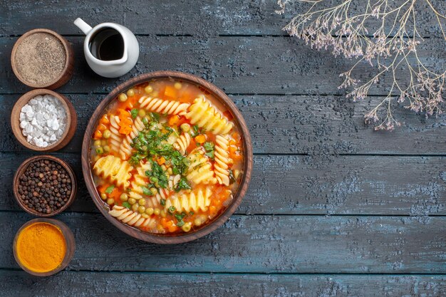 Vue de dessus délicieuse soupe de pâtes à base de pâtes en spirale avec assaisonnements sur la sauce de bureau bleu foncé plat de cuisine soupe de pâtes italiennes