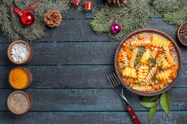 Vue de dessus une délicieuse soupe de pâtes à partir de pâtes italiennes en spirale avec des assaisonnements sur le bureau bleu foncé cuisine plat de couleur pâtes à soupe