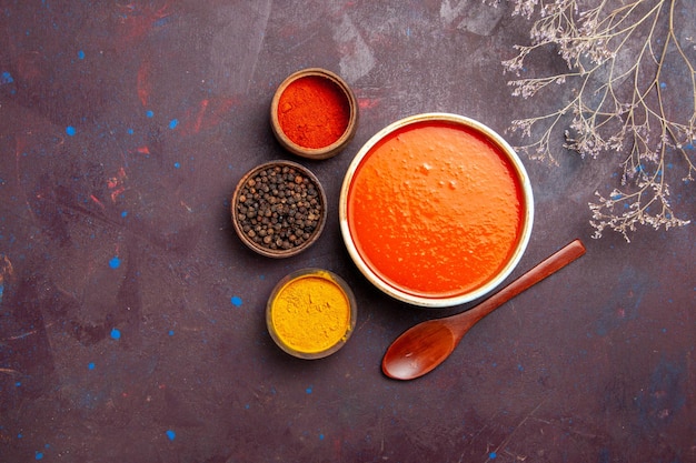 Vue de dessus délicieuse soupe de tomate cuite à partir de tomates fraîches avec assaisonnements sur fond sombre sauce repas plat de tomate soupe