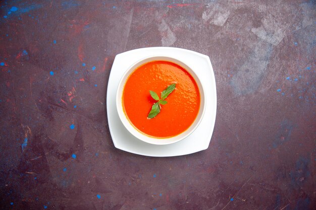 Vue de dessus délicieuse soupe de tomate plat savoureux avec une seule feuille à l'intérieur de la plaque sur un fond sombre sauce plat couleur tomate soupe de dîner