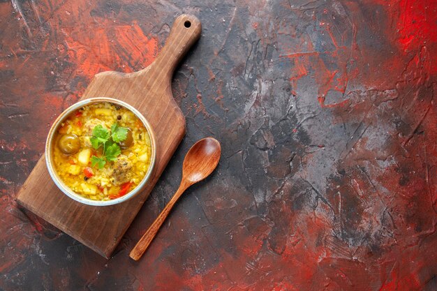 Vue de dessus une délicieuse soupe de viande à l'intérieur d'une petite assiette sur une planche à découper fond rouge foncé plat de légumes cuisine repas cuisine nourriture viande cuisinier place libre