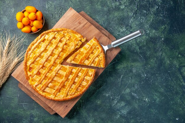 Vue de dessus de la délicieuse tarte au kumquat avec un morceau en tranches sur une surface sombre