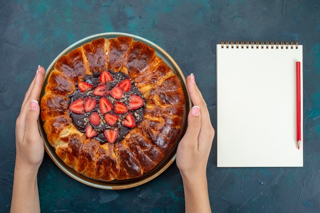 Vue de dessus de la délicieuse tarte aux fraises avec bloc-notes sur une surface bleu foncé