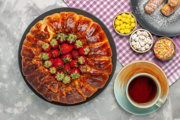 Vue de dessus de la délicieuse tarte aux fraises avec des fraises rouges fraîches et une tasse de thé sur une surface blanche