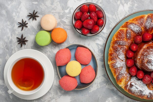 Vue de dessus délicieuse tarte aux fraises avec petits gâteaux macarons et tasse de thé sur la surface blanche gâteau tarte biscuit thé au sucre sucré cuire