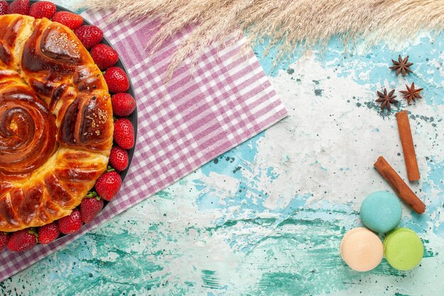 Vue de dessus délicieuse tarte aux fraises rouges et macarons sur surface bleue
