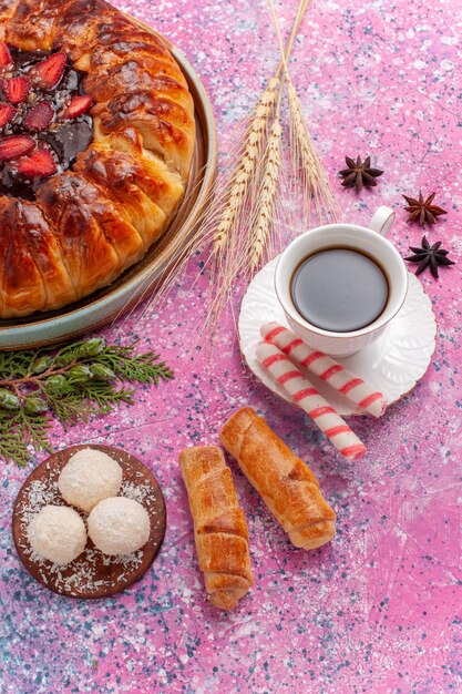 Vue de dessus délicieuse tarte aux fraises avec une tasse de thé sur le bureau rose