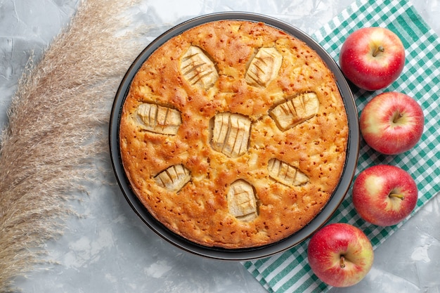 Photo gratuite vue de dessus délicieuse tarte aux pommes sucrée cuite à l'intérieur de la poêle avec des pommes rouges sur le bureau blanc